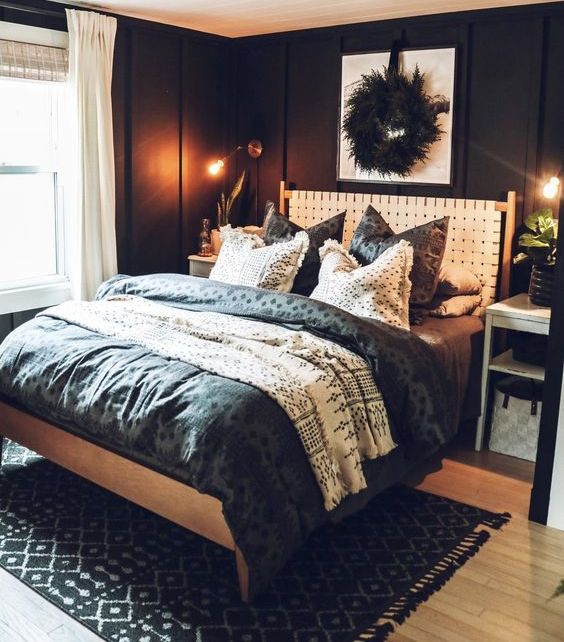 a black bedroom with paneling, a bed with a white leather headboard, black and white bedding, a feather wreath and white textiles