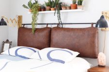 a boho bedroom with a brown leather suspended headboard, printed bedding, a shelf with potted plants