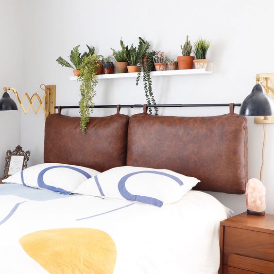 a boho bedroom with a brown leather suspended headboard, printed bedding, a shelf with potted plants