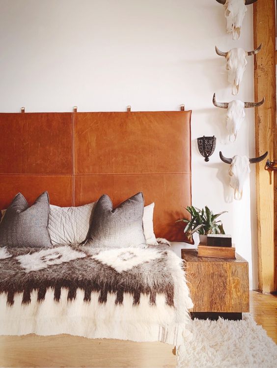 a boho bedroom with an amber leather suspended headboard, a bed with printed bedding, a skull gallery wall