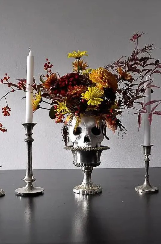 a bold Halloween centerpiece of a bowl holding a skull with super bright blooms, candlesticks and tall and thin candleholders