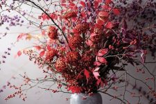 a catchy Halloween centerpiece of a vase with bold red blooms, leaves and branches with berries is bright and cool