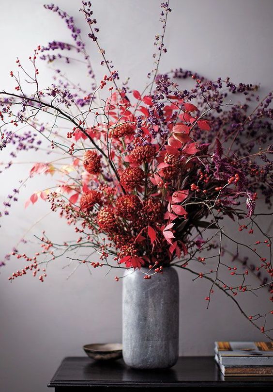 a catchy Halloween centerpiece of a vase with bold red blooms, leaves and branches with berries is bright and cool