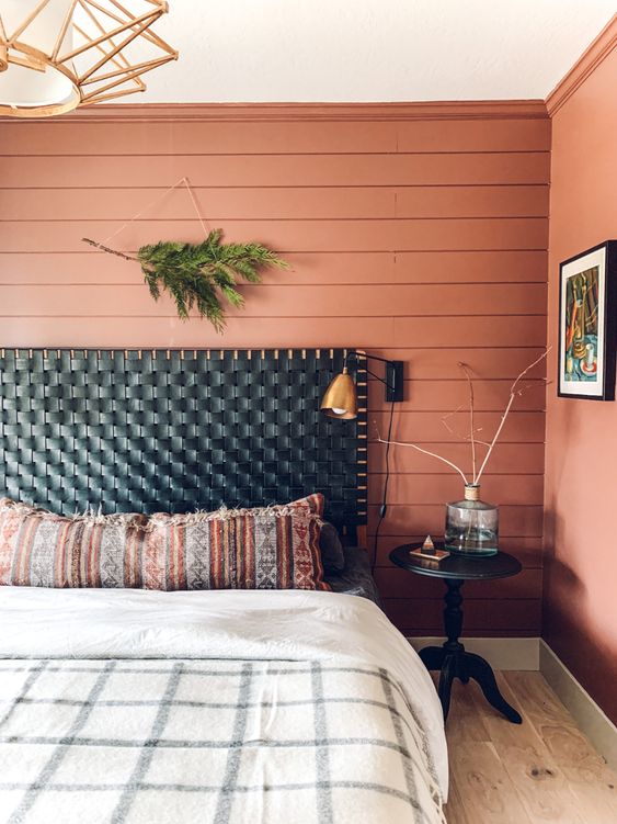 a catchy boho bedroom with a salmon pink accent wall, a bed with a black woven headboard, printed bedding, a black nightstand