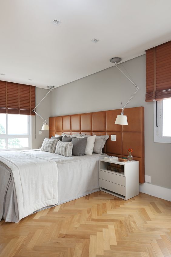 a chic modern bedroom with grey walls, a bed with an amber leather headboard, ceiling lamps, nightstands and shades