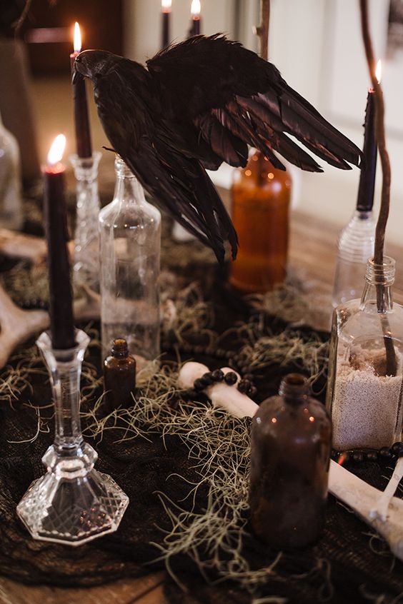 a cluster Halloween centerpiece of hay, bottles, black candles and a blackbird is a cool solution