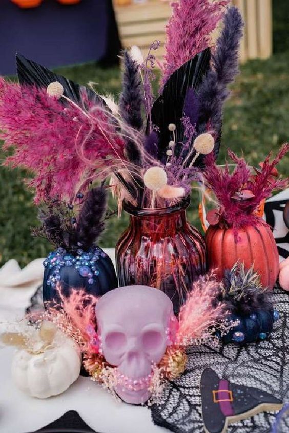 a colorful Halloween centerpiece of a pink skull, pink and black vases with feathers and leaves and a small white pumpkin