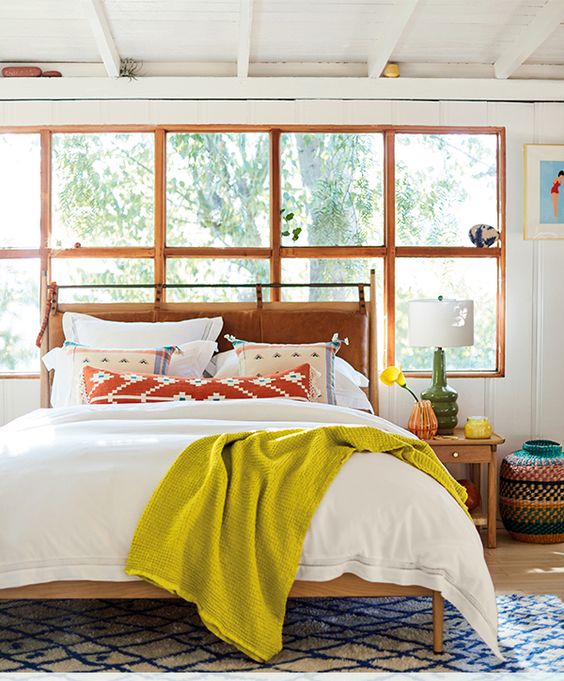 a colorful bedroom with a bed and a leather hanging headboard, bold bedding, a printed rug, and some colorful decor