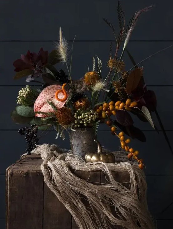 a creepy floral Halloween centerpiece with dark foliage, grasses, kumquats, berries and leaves
