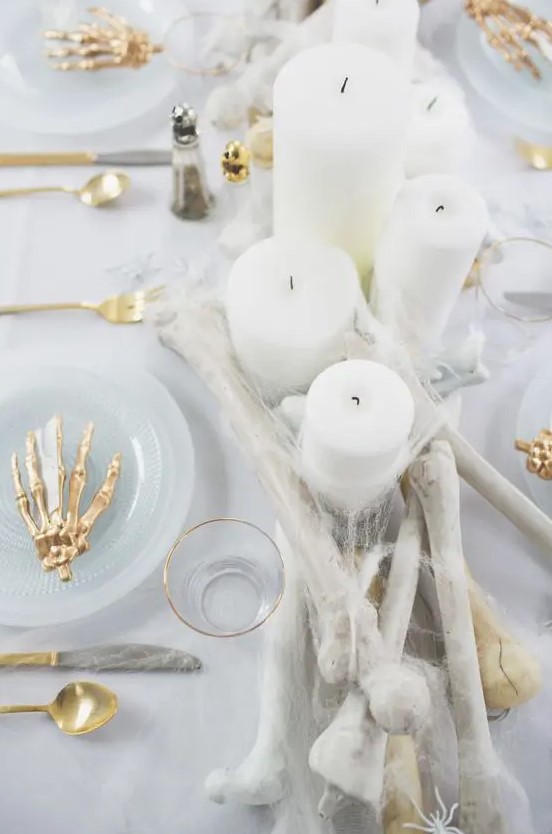 a glam Halloween table setting done in white, with bones, gold skeleton hands, candles and spiderwebs