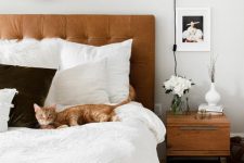 a mid-century modern bedroom with a brown leather bed, monochromatic bedding, stained nightstands, a sconce and some decor