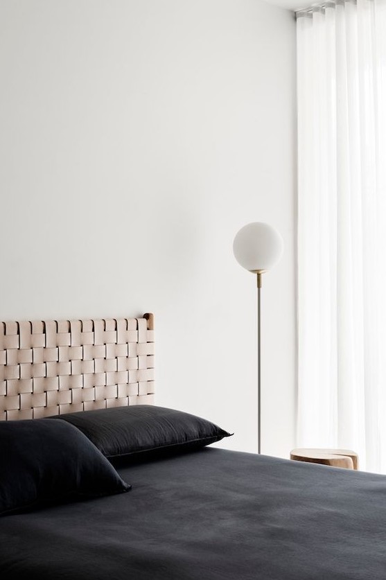 a minimalist bedroom with a woven headboard that adds interest to the sleek space and contrasts black bedding