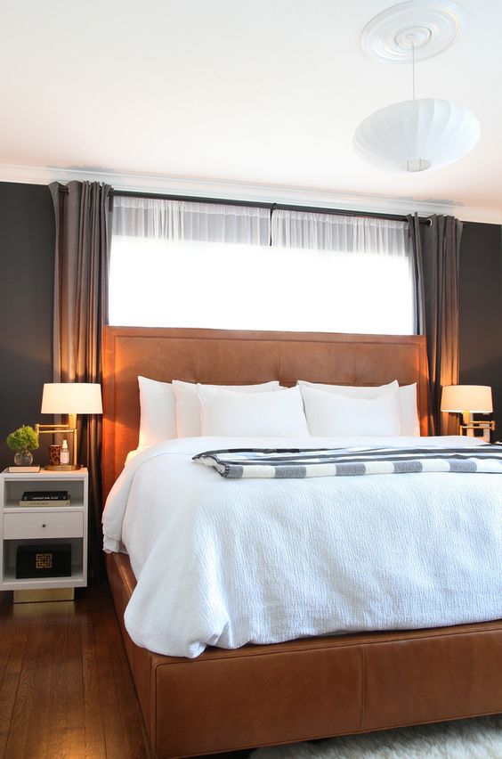 a modern bedroom with black walls, an amber leather bed, white nightstands and neutral bedding