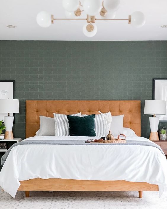 a modern bedroom with green brick walls, a bed with an amber leather headboard, white nightstands and table lamps