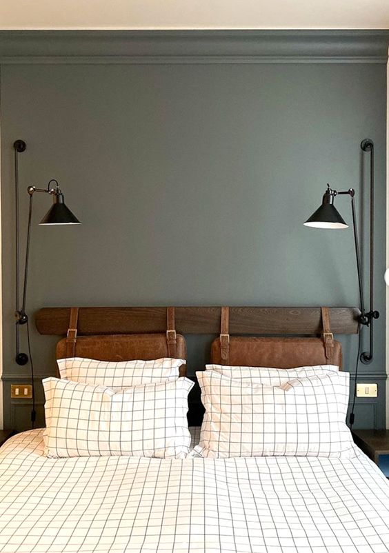 a modern bedroom with grey walls, a bed with brown leather suspended headboard, printed bedding and black lamps