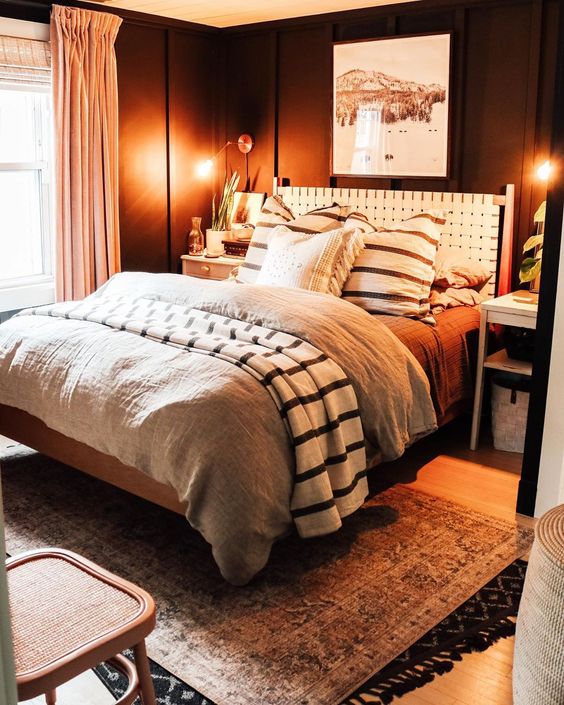 a moody boho bedroom with black walls, a bed with a white leather headboard, printed bedding, a boho rug and some decor