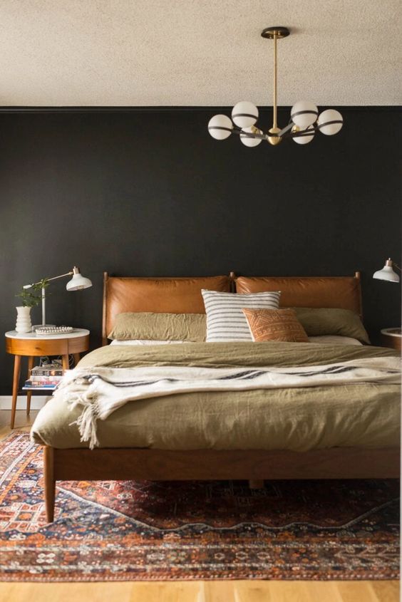 a moody mid-century modern bedroom with black walls, a bed with an amber leather headboard and muted color bedding and a nightstand