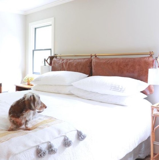 a neutral and serene space done with a brown leather pillow headboard on a brass holder that adds color and texture