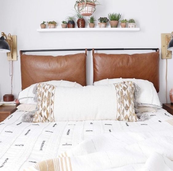 a neutral bed with embroidered and tasseled bedding and brown leather pillows as a headboard