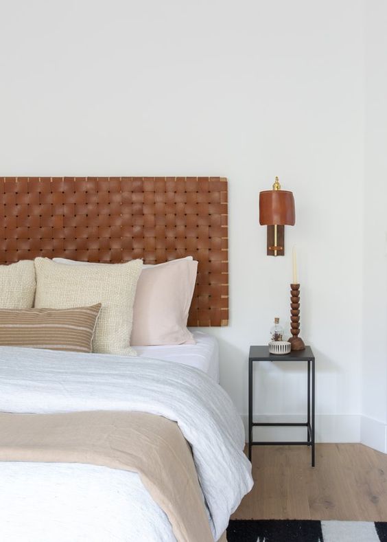 a neutral boho bedroom with a brown woven leather headboard and neutral bedding, a black nightstand and a sconce