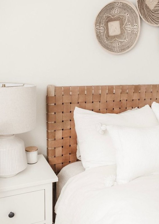 a neutral boho bedroom with decorative baskets, a bed with a woven leather headboard and neutral furniture