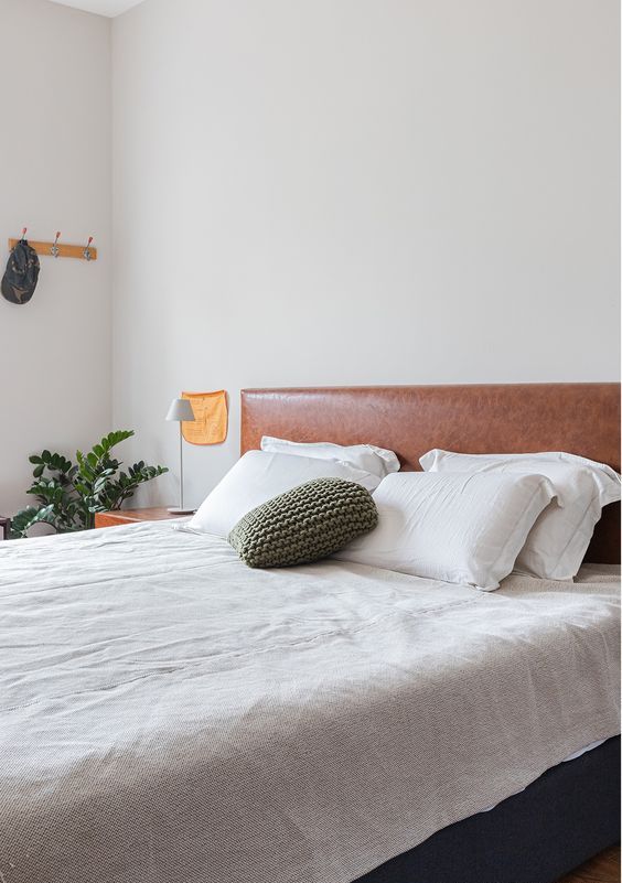 a neutral modern bedroom with a bed and a brown leather headboard, neutral bedding, nightstands, table lamps and greenery