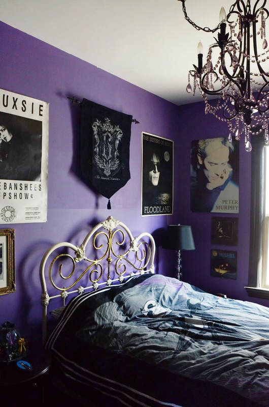 a purple and black bedroom with a bold gallery wall, a forged bed, a black crystal chandelier and a black lamp is gorgeous