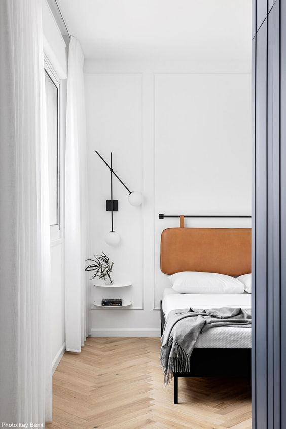 a refined modern bedroom with a bed and an amber leather suspended headboard, neutral bedding, floating nightstands and lamps