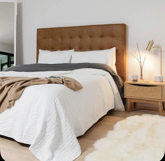 a serene bedroom with a bed and an extended amber leather tufted headboard, neutral textiles and a nightstand