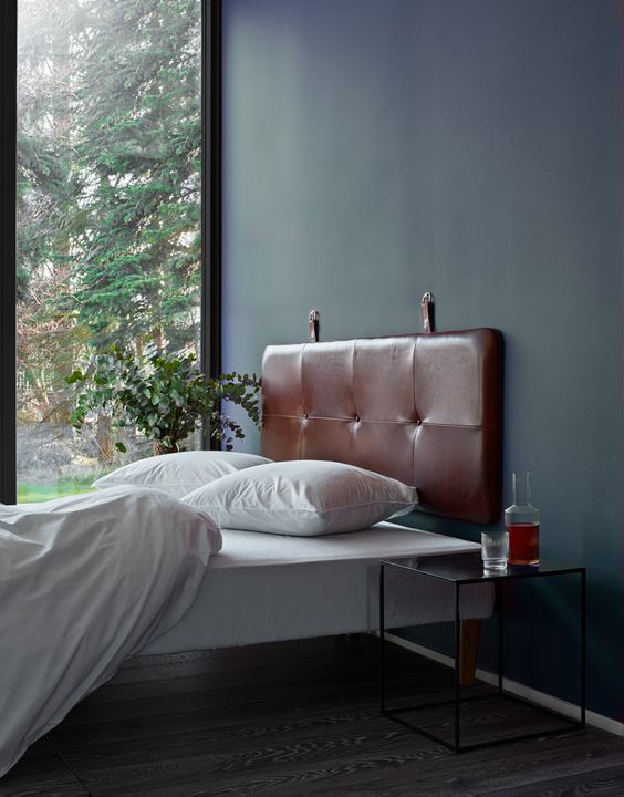 a serene bedroom with dark walls, a bed with a brown suspended headboard, white bedding, nightstands and greenery