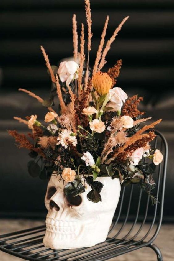 a skull with neutral blooms, greenery and dried grasses is a cool and pretty Halloween centerpiece