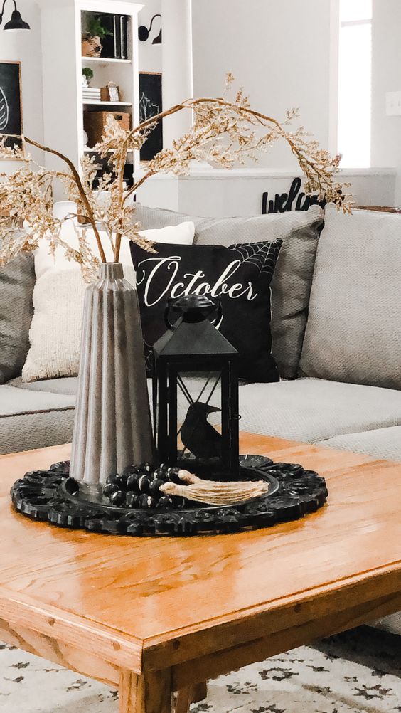 a stylish Halloween centerpiece of a tray, a concrete vase with branches, a black lantern with a bird is cool