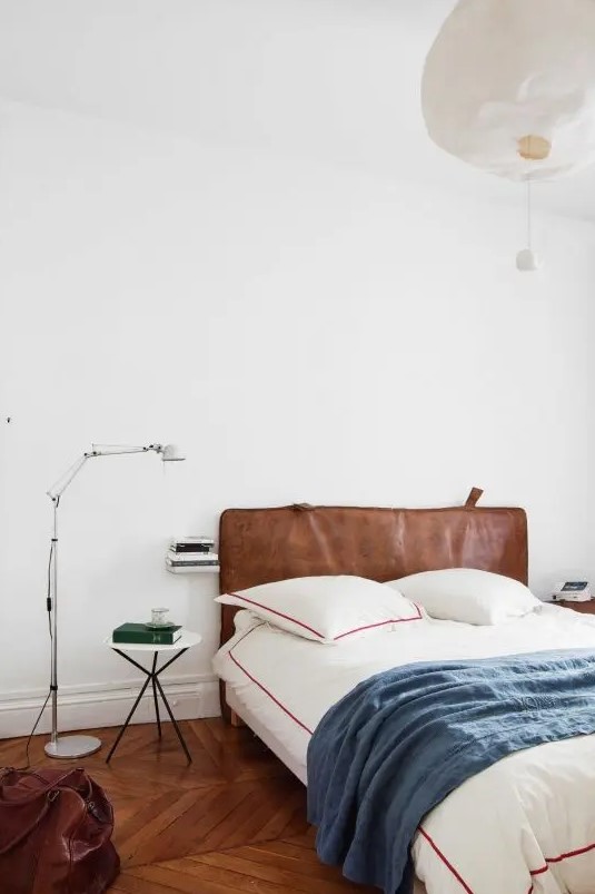 an eclectic bedroom wiht a bed and a brown leather headboard, printed bedding, a small nightstand, a floor lamp and some decor