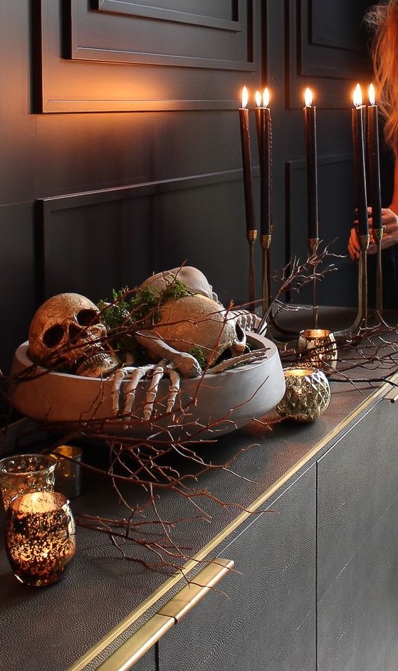 refined Halloween decor with a bowl filled with skeleton hands, skulls and moss, branches, candles around is amazing