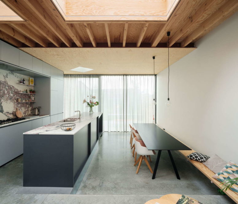 The kitchen features grey cabinets, a pink stone backsplash and a countertop plus a simple dining space with a table, a bench and chairs The kitchen features grey cabinets, a pink stone backsplash and a countertop plus a simple dining space with a table, a bench and chairs