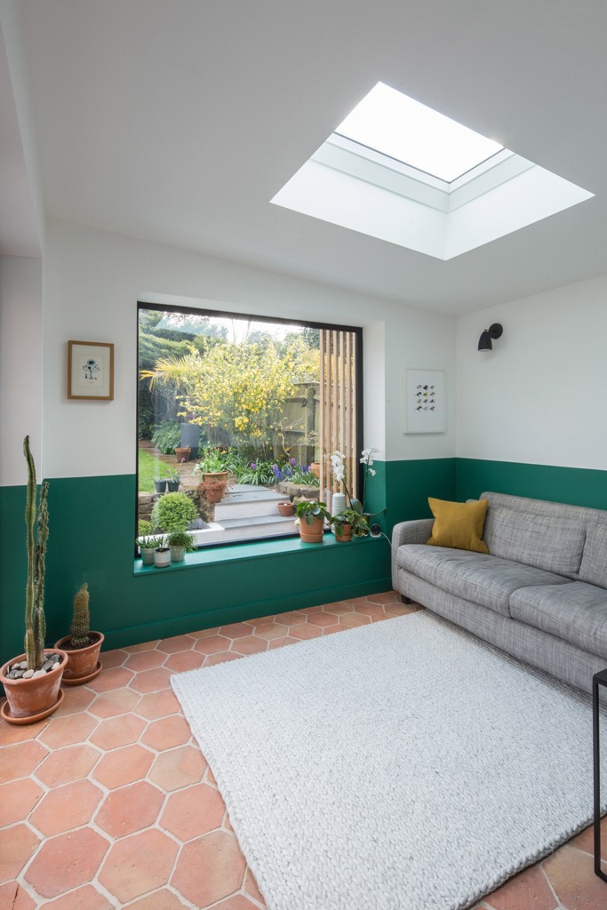The living room features colo color blocking an emerald and white wall and it is filled with light through a window and a skylight The living room features colo color blocking - an emerald and white wall and it is filled with light through a window and a skylight