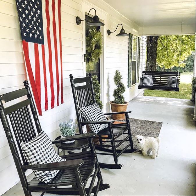 The porch is done with cozy black rockers, a hanging daybed, some potted greenery and lamps over the door The porch is done with cozy black rockers, a hanging daybed, some potted greenery and lamps over the door