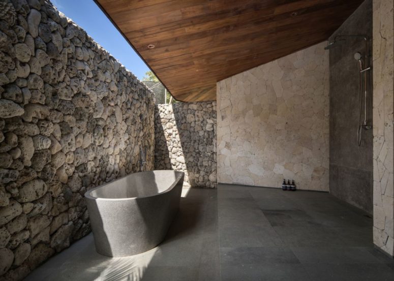 a stone bathroom design with a wooden roof the bathroom with a shower and a tube of stone is indoor-outdoor with a stone wall that keeps privacy and a roof over it