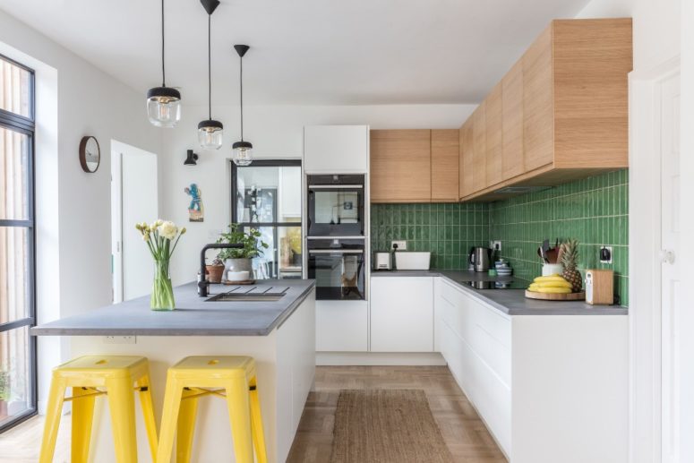 a modern kitchen island with a concrete countertop The kitchen is done with sleek cabinets and a green tile backsplash, a kitchen island with a concrete countertop and bright yellow stools