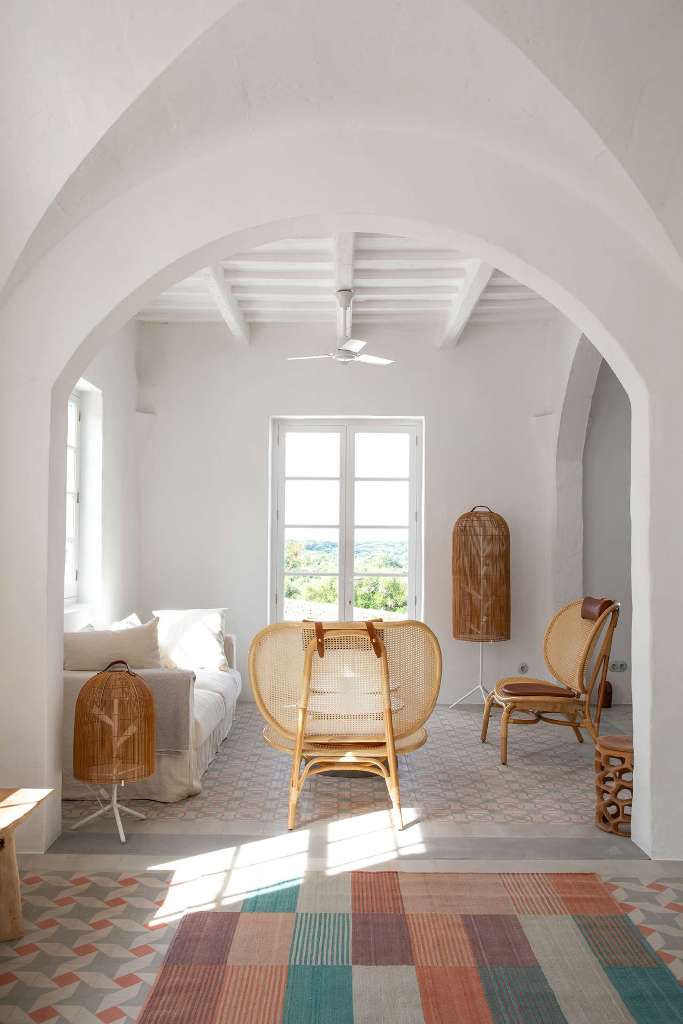 The living room is done with rattan furniture, a white sofa, pretty tiles and rugs and looks very Spanish-like