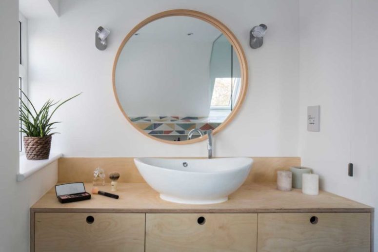 The bathroom is done with a plywood vanity, an oval sink and a round mirror