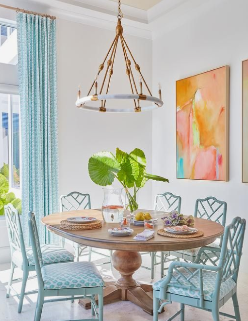 a white dining space infused with color using blue curtains and chairs and bright artworks on the wall