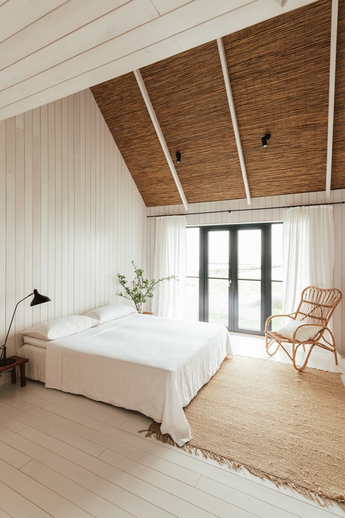 The bedroom is done with white plywood walls, an attic ceiling, a jute rug and a rattan chair plus some greenery and a glazed wall The bedroom is done with white plywood walls, an attic ceiling, a jute rug and a rattan chair plus some greenery and a glazed wall