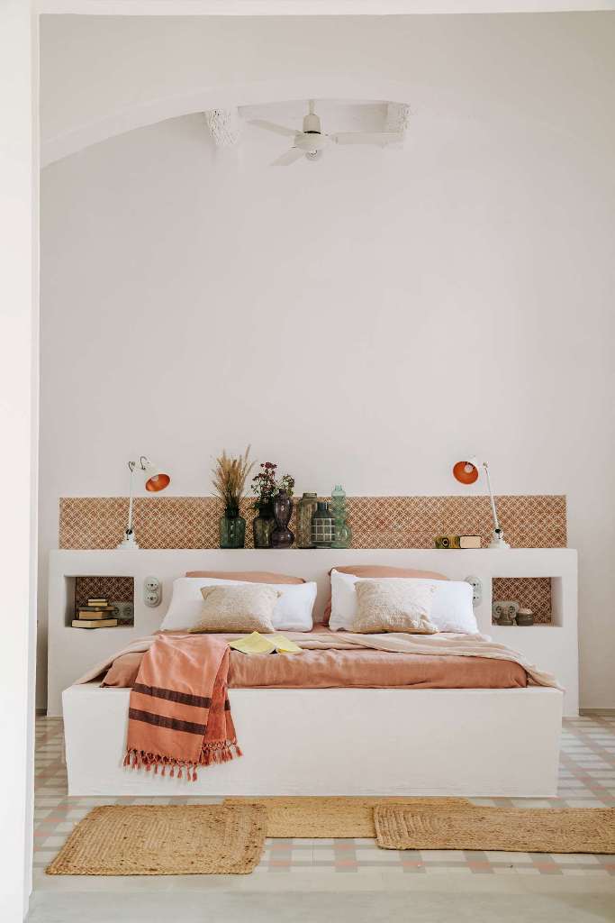 The bedroom is done  with a storage headboard, lots of rugs, pretty tiles on the wall and coral bedding