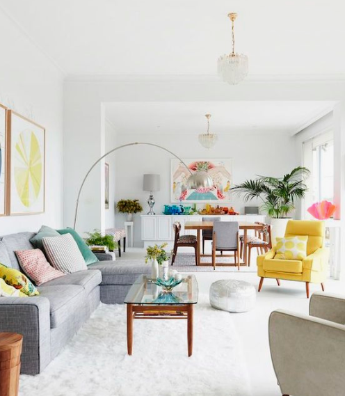 a white open space with a living room and a kitchen spruced up with colorful pillows, artworks and a yellow chair
