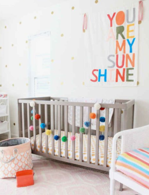 an all-neutral nursery with a colorful artwork, a bright pompom garland and a colorful striped chair