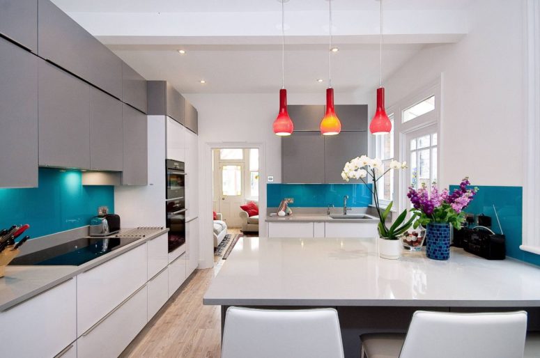 a minimalist open layout refreshed with bright blue ktchen backsplashes and bold red pendant lamps over the table