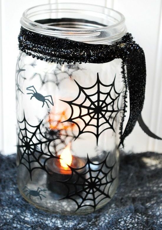 a sheer mason jar decorated with blakc spiderwebs and spiders plus a black glitter ribbon will be a nice candleholder