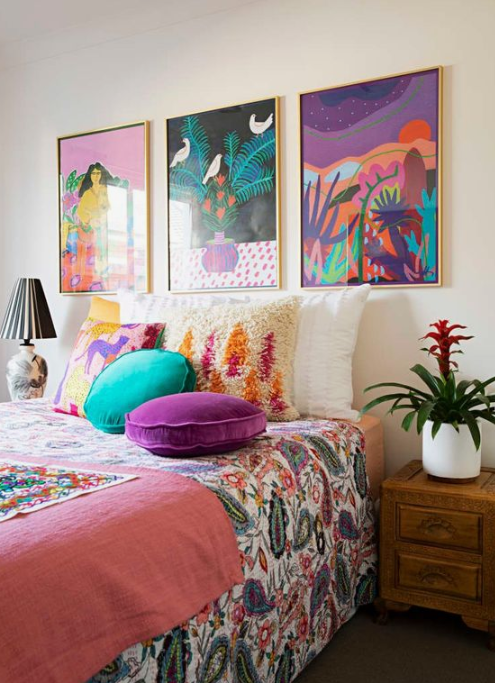 a colorful bedroom done in turquoise and purple, with colorful artworks over the bed, printed bedding and pillows