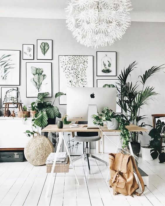 a chic neutral home office with a large gallery wall, potted greenery and plants, a trestle desk and some vintage suitcases